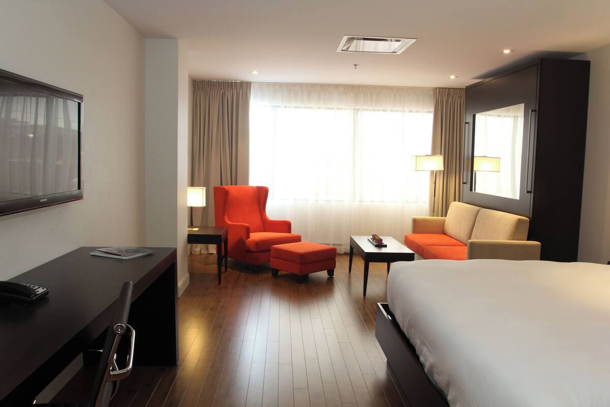 A hotel room with a bed, a desk, a chair, a sofa, and a TV.