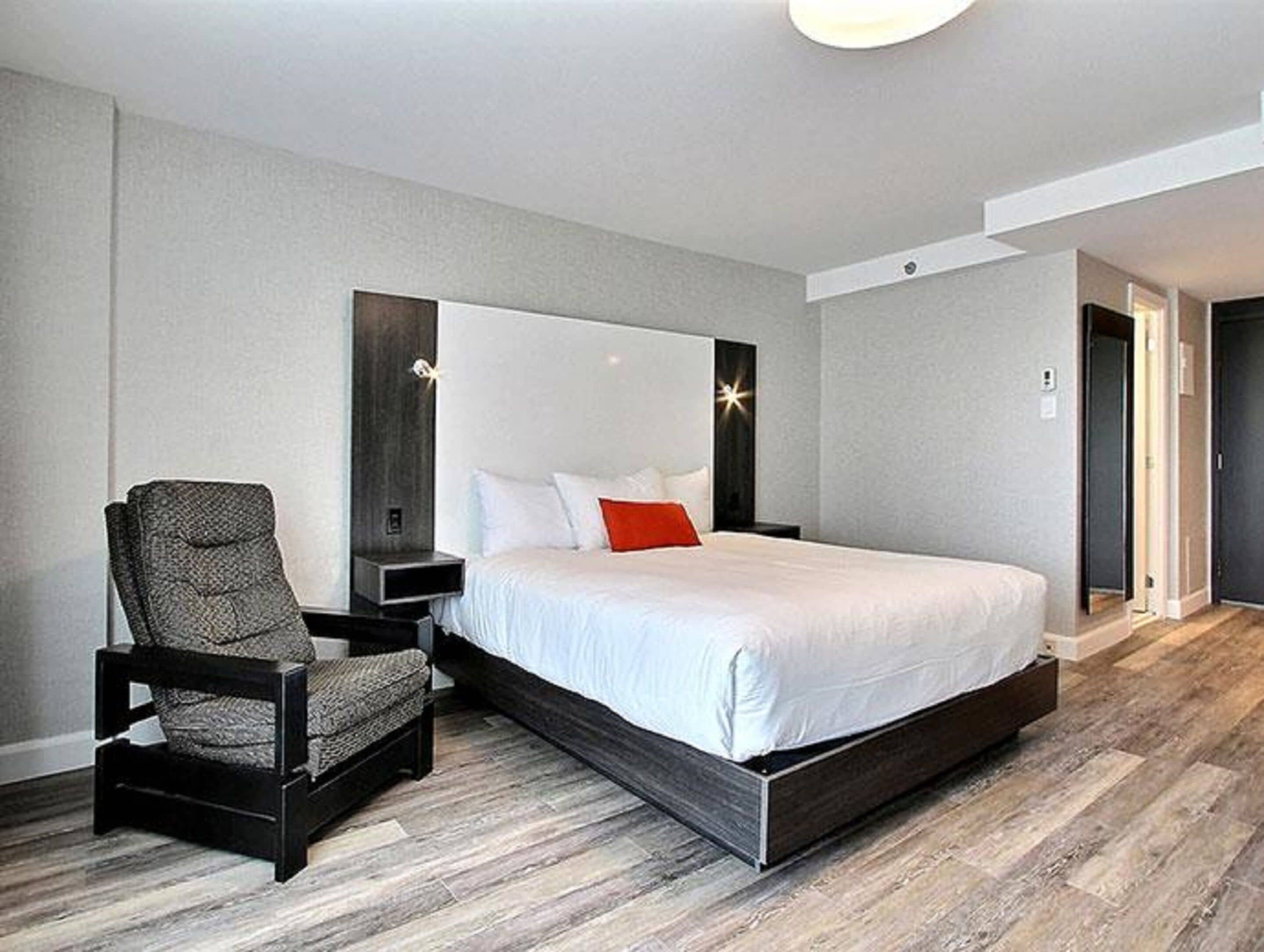 A modern bedroom with a large bed, a chair, and a nightstand.