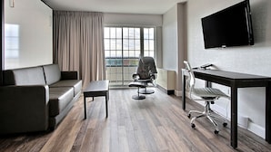 A modern hotel room with a sofa, a desk, a chair, a TV, and a large window with curtains. - Hotel Classique (Québec City)