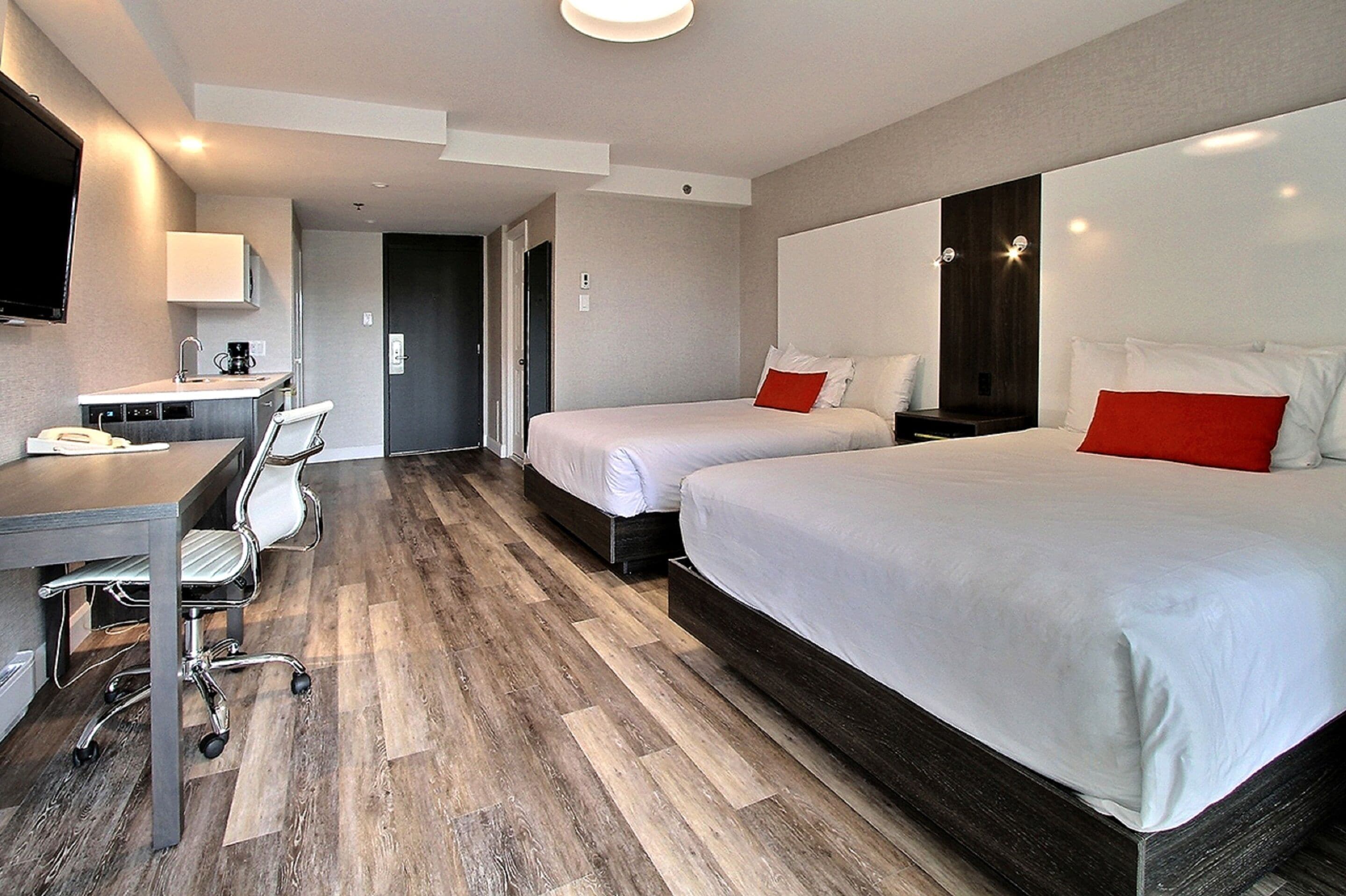 A hotel room with a desk, two beds, a TV, and a wooden floor.