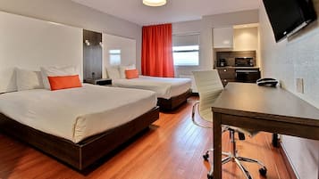 A hotel room with two beds, a desk, a chair, a TV, and a kitchenette.