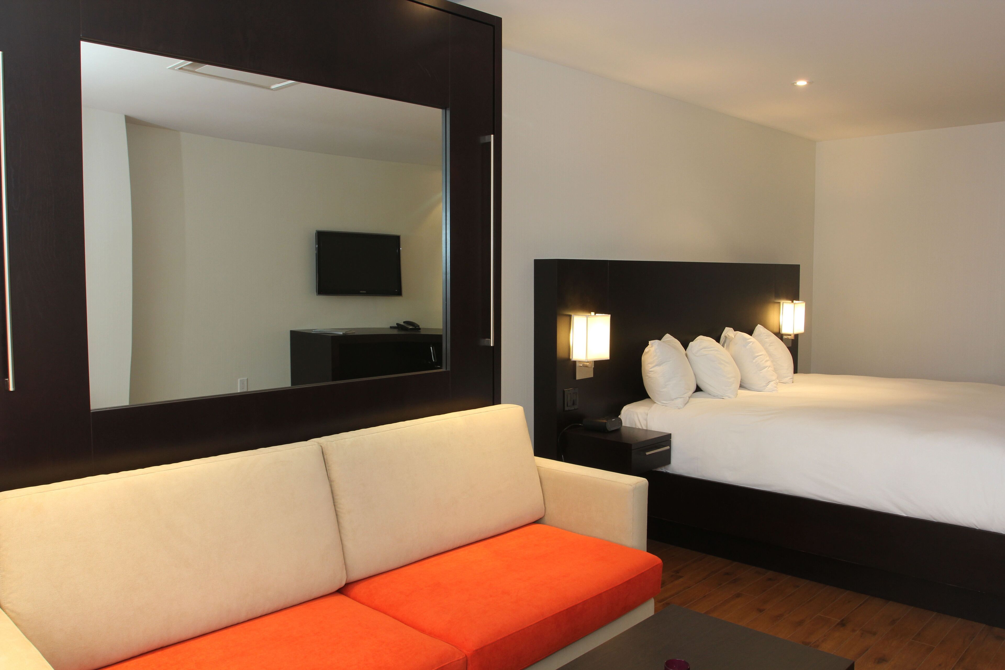Quarto de hotel com uma cama grande, um sofá, uma televisão e um espelho.