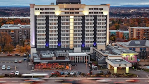 A multi-story hotel with a modern design, featuring a prominent entrance and a parking lot with several cars. - Hotel Classique (Québec City)