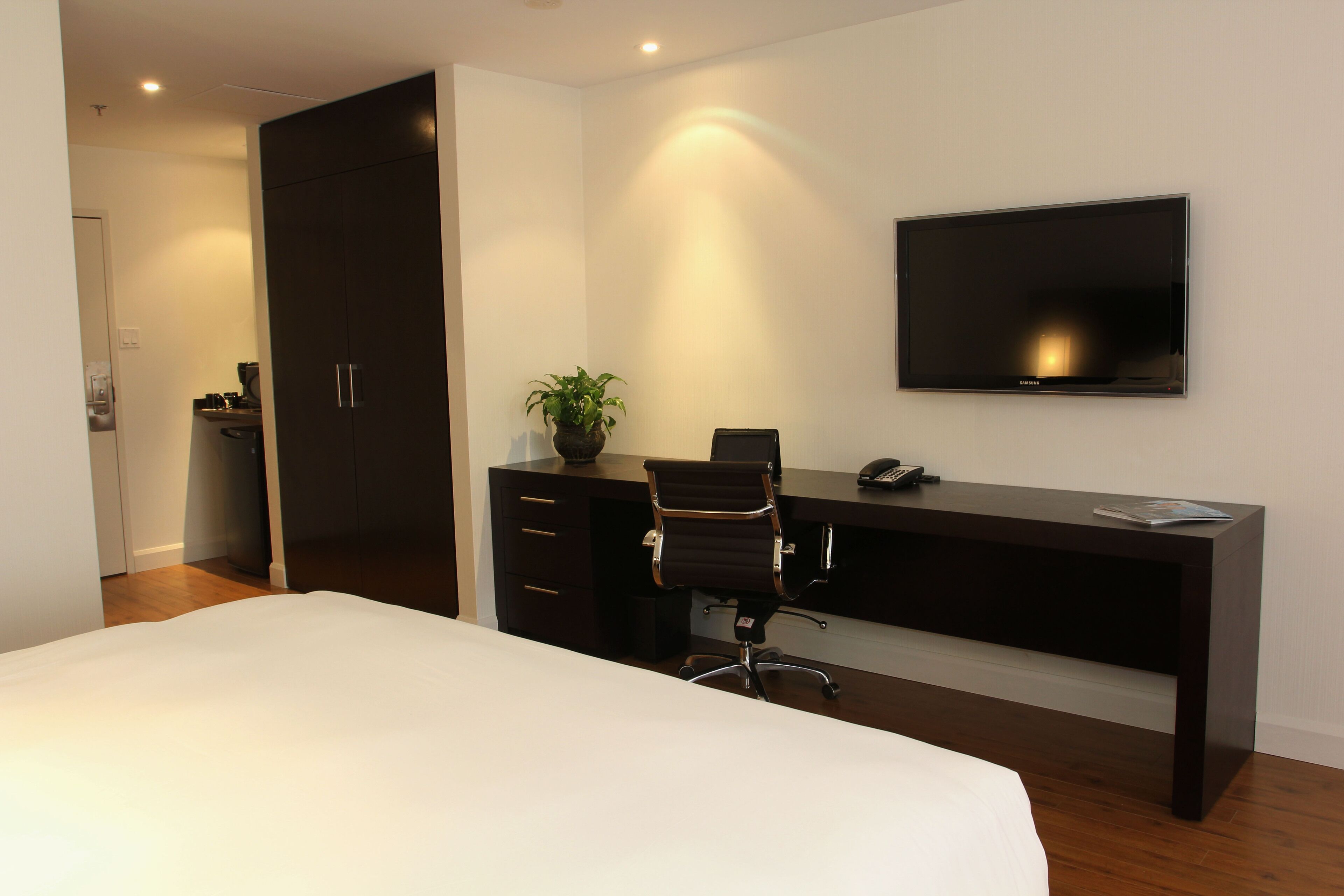 Habitación de hotel con cama, escritorio, silla, televisor y armario.