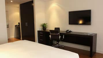 Habitación de hotel con cama, escritorio, silla, televisor y armario.