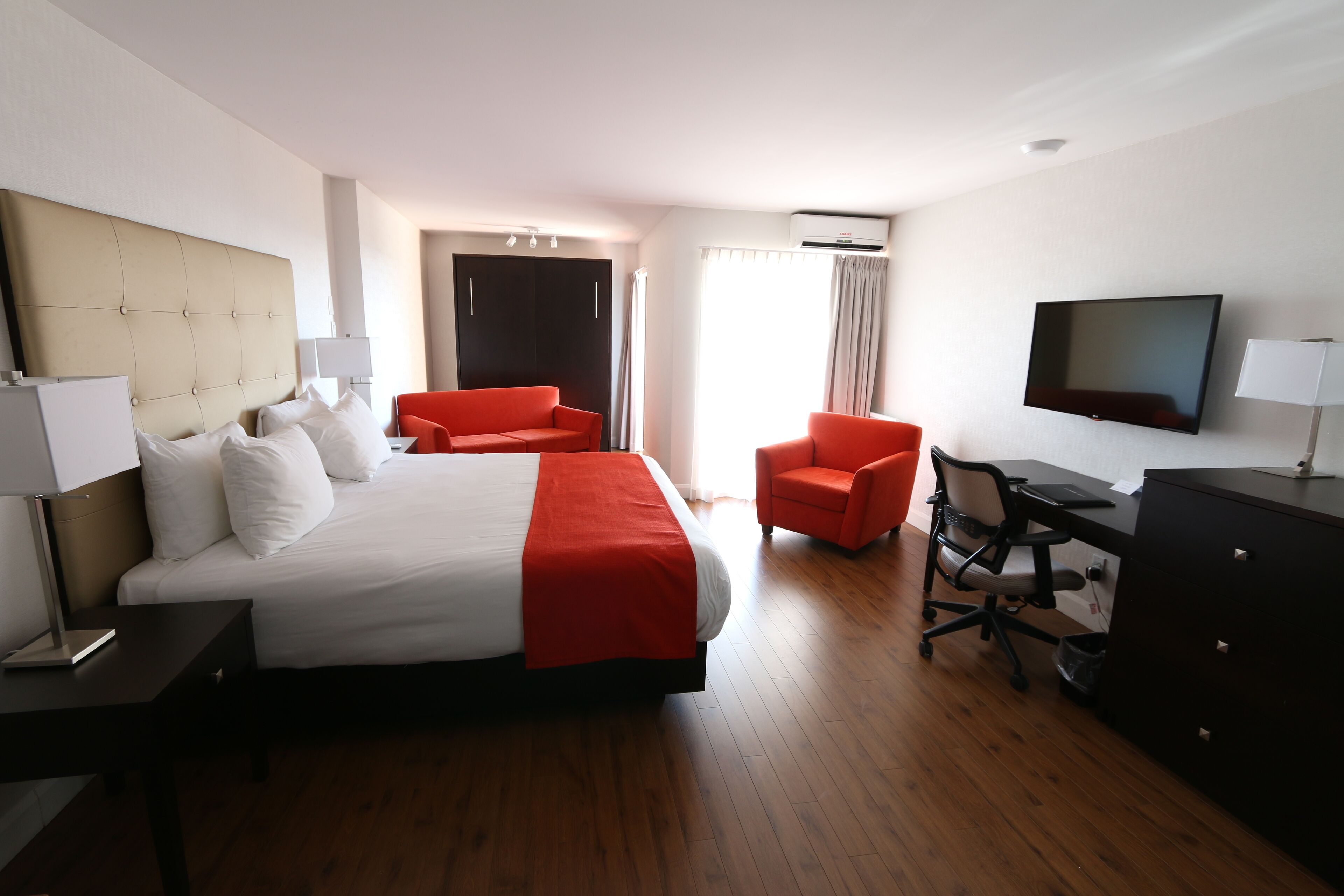 Quarto de hotel com uma cama grande, uma escrivaninha, uma cadeira, uma televisão e um guarda-roupa.