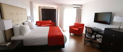 A hotel room with a large bed, a desk, a chair, a TV, and a wardrobe.