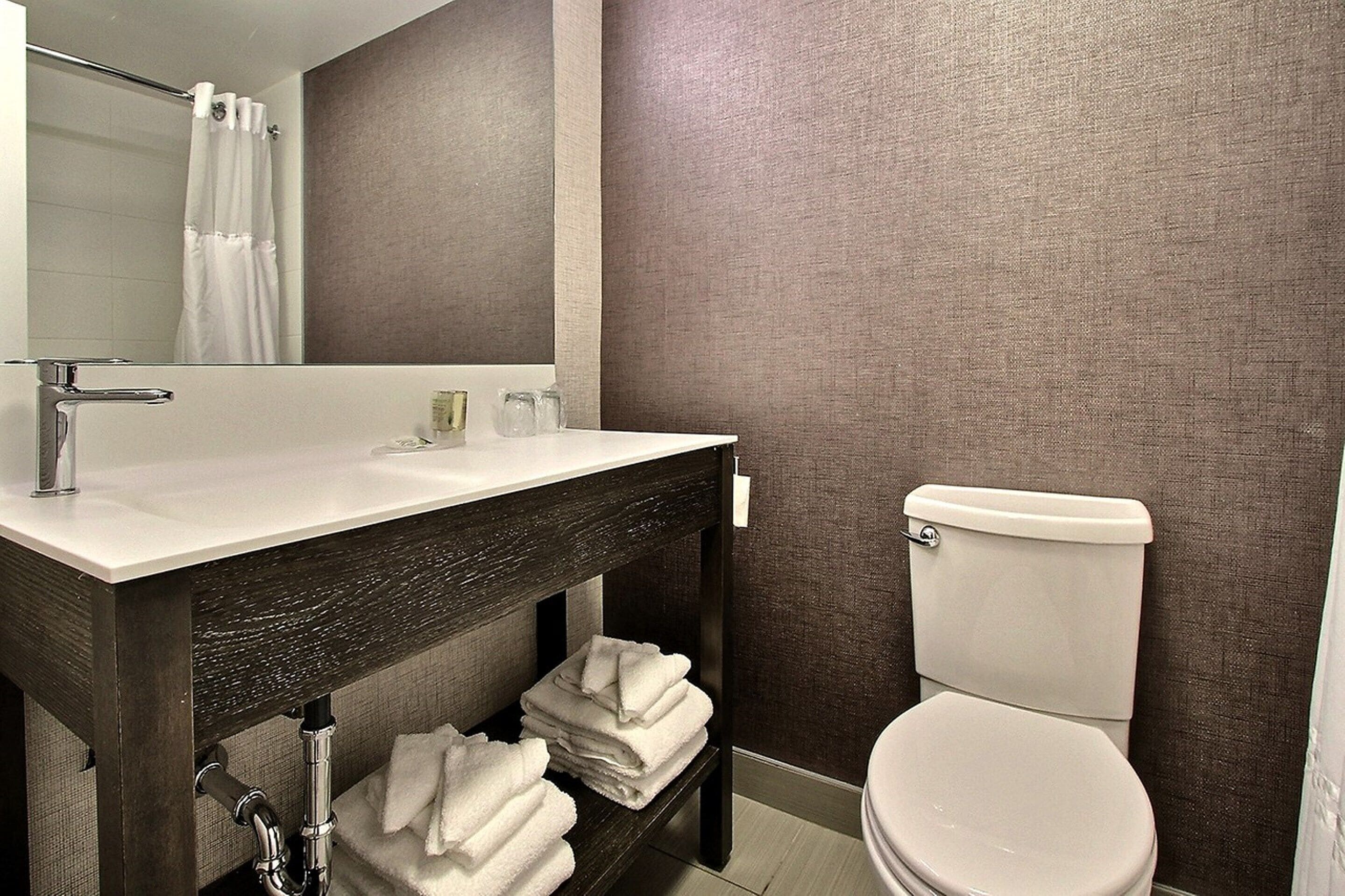 Un baño con lavamanos blanco, tocador de madera oscura, espejo, inodoro y cortina de ducha.