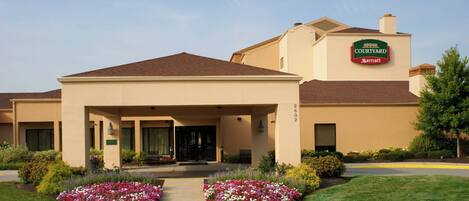 A Courtyard Marriott hotel with a covered entrance, landscaped flower beds, and a clear sky.