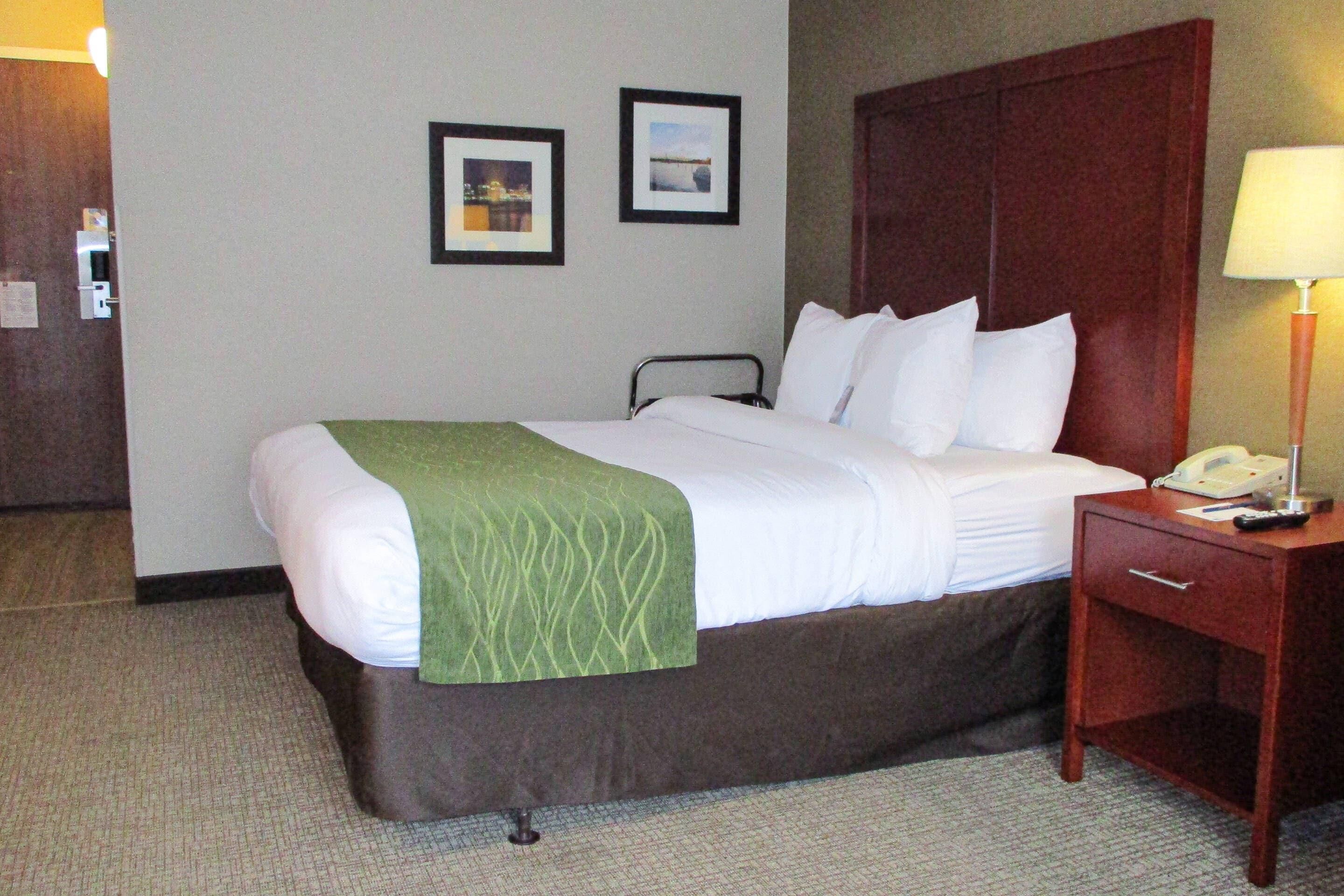 A hotel room with a bed, a nightstand with a lamp, and two framed pictures on the wall.