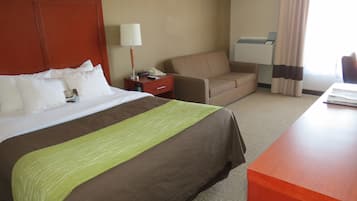 A hotel room with a large bed, a desk, a chair, a nightstand, and a lamp.