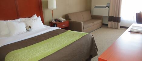 Una habitación de hotel con una cama grande, un escritorio, una silla, una mesita de noche y una lámpara.