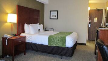 A hotel room with a bed, bedside table, lamp, and a chair.