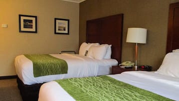 A hotel room with two beds, a nightstand with a lamp, and framed pictures on the wall.