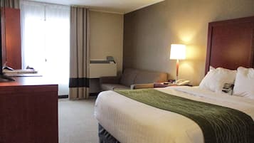 Une chambre d’hôtel avec un lit, un bureau, une chaise, une lampe et une fenêtre avec des rideaux.