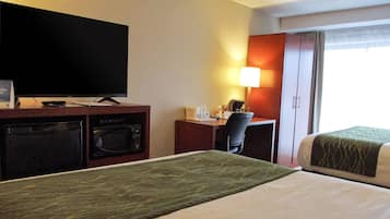 Una habitación de hotel con una cama, un escritorio con lámpara, televisión y microondas.