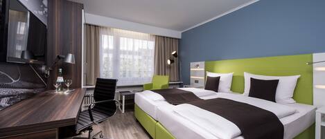 Habitación de hotel con una cama grande, un escritorio con silla, un televisor y una ventana con cortinas.
