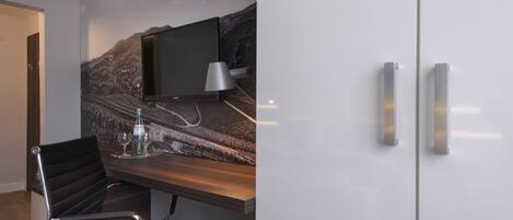 Ein modernes Hotelzimmer mit einem an einer strukturierten Wand befestigten Flachbildfernseher, einem Holztisch mit Stuhl und einer Minibar.