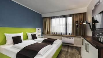 A hotel room with a bed, bedside table, lamp, and a view of the city through the window.