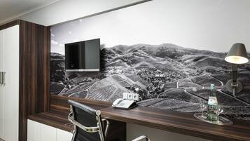 Ein moderner Büroraum mit Schreibtisch, Stuhl, Wandfernseher und Wandgemälde mit Landschaftsmotiv.