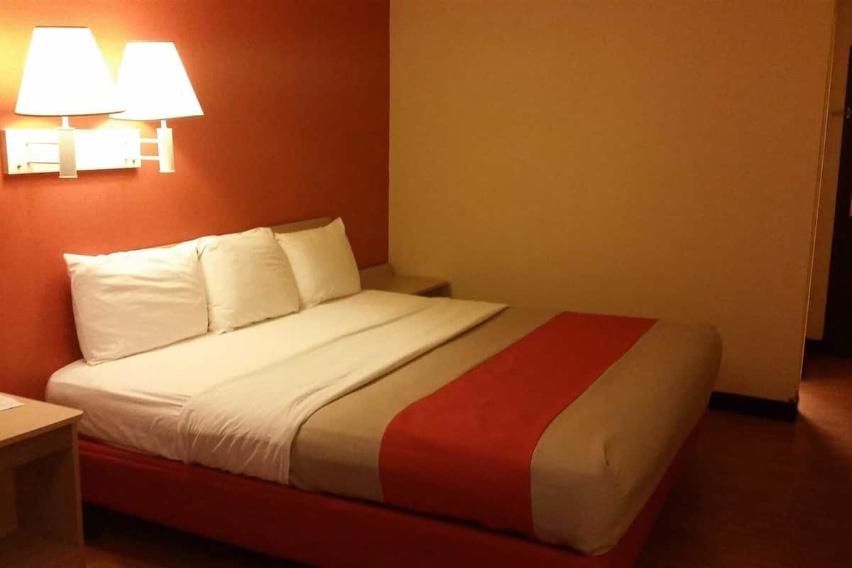 Een hotelkamer met een bed, nachtkastje en een wandlamp.