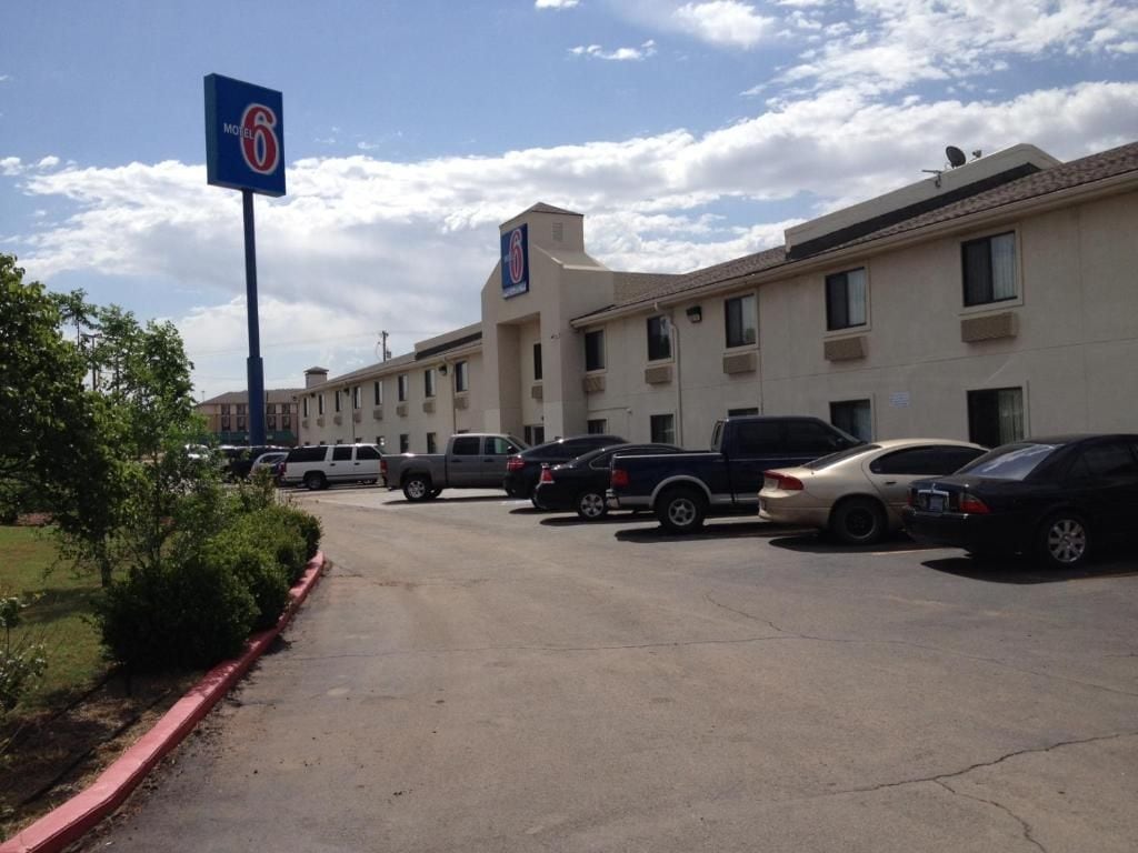 A motel with a parking lot, a signboard, and a building with multiple windows.