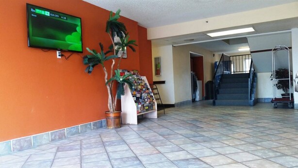 Un hall d’entrée avec un sol carrelé, un téléviseur fixé au mur, un escalier et un présentoir contenant des brochures.