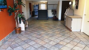 Un hall d’hôtel avec un sol carrelé, un comptoir d’accueil, un escalier et des plantes en pot.