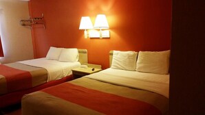 Une chambre d’hôtel avec deux lits, une table de chevet avec une lampe et un mur rouge.