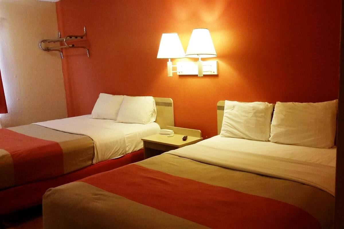 Een hotelkamer met twee bedden, een nachtkastje met een lamp en een rode muur.