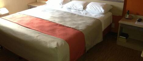 A single bed with a white and red bedspread, a wooden floor, and a small bedside table with a lamp.