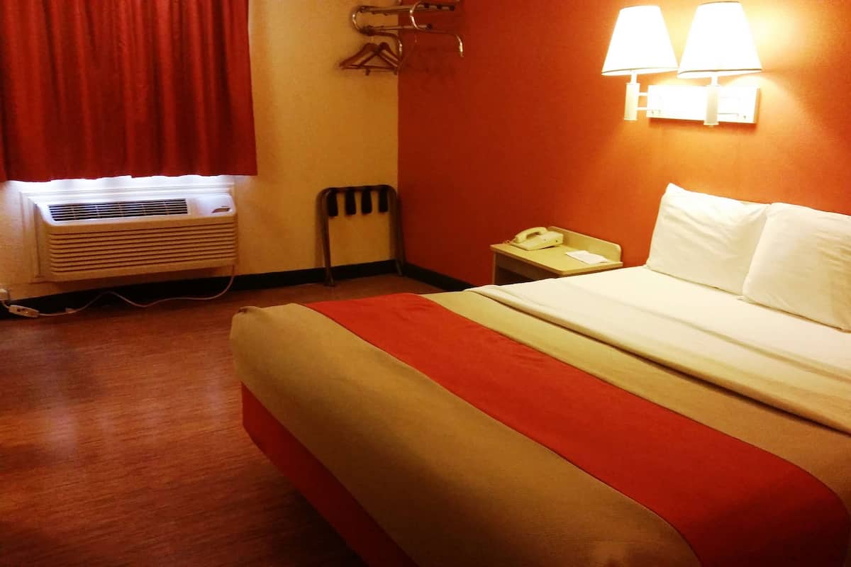 Een hotelkamer met een bed, nachtkastje met lamp, verwarming en telefoon.
