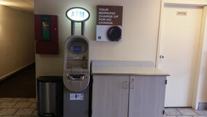 Un distributeur automatique de billets, une poubelle et un panneau indiquant qu’une recharge gratuite est possible le matin.