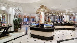 A luxurious lobby with marble flooring, a central decorative column, and a glass staircase.
