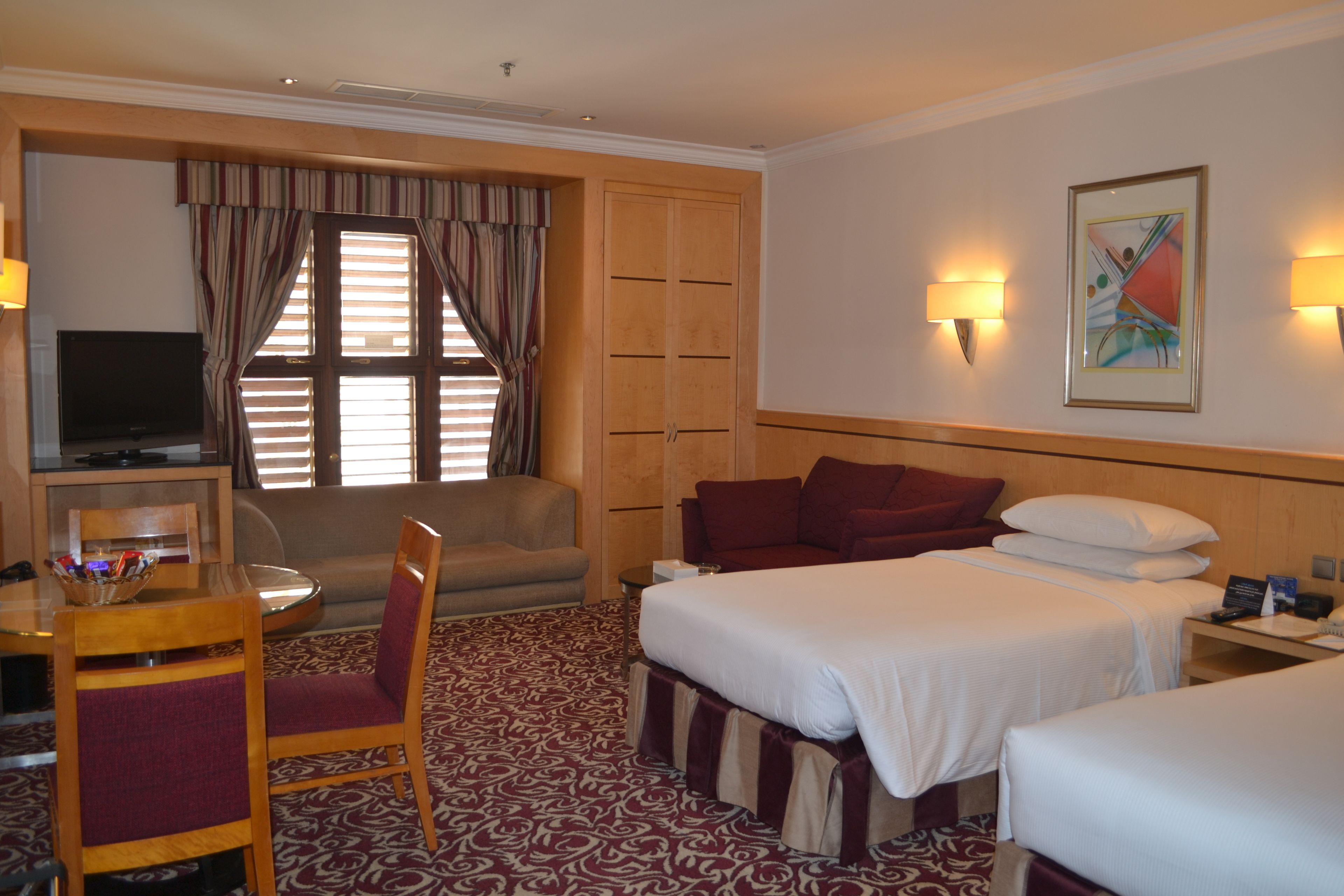 Habitación de hotel con cama, dos mesitas de noche, escritorio con silla, televisión y ventana con cortinas.