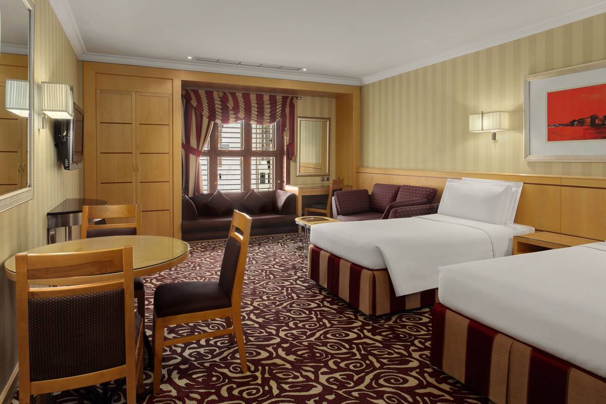 A hotel room with two beds, a sofa, a dining table, and a chair.