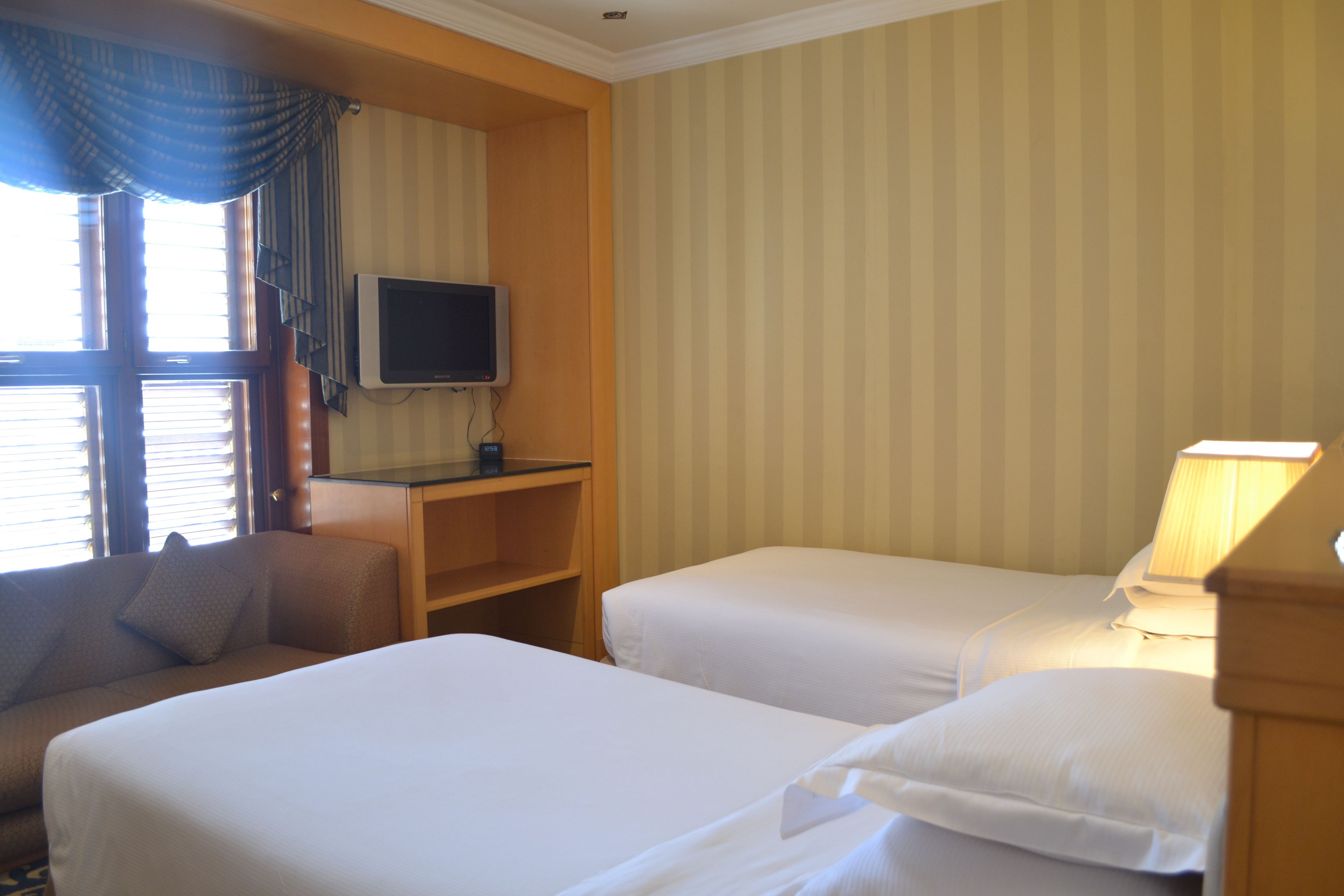 A hotel room with two beds, a TV, a desk, and a lamp.