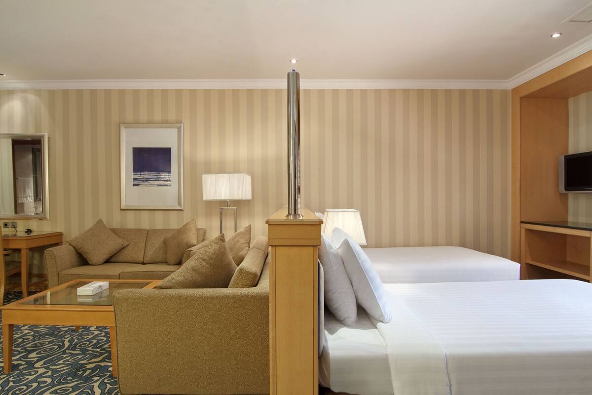 A hotel room with a sofa, two single beds, a lamp, a TV, and a framed picture on the wall.