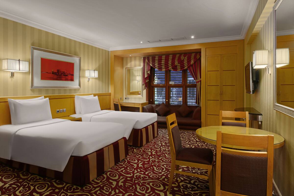 A hotel room with two beds, a sofa, a dining table, and a TV.