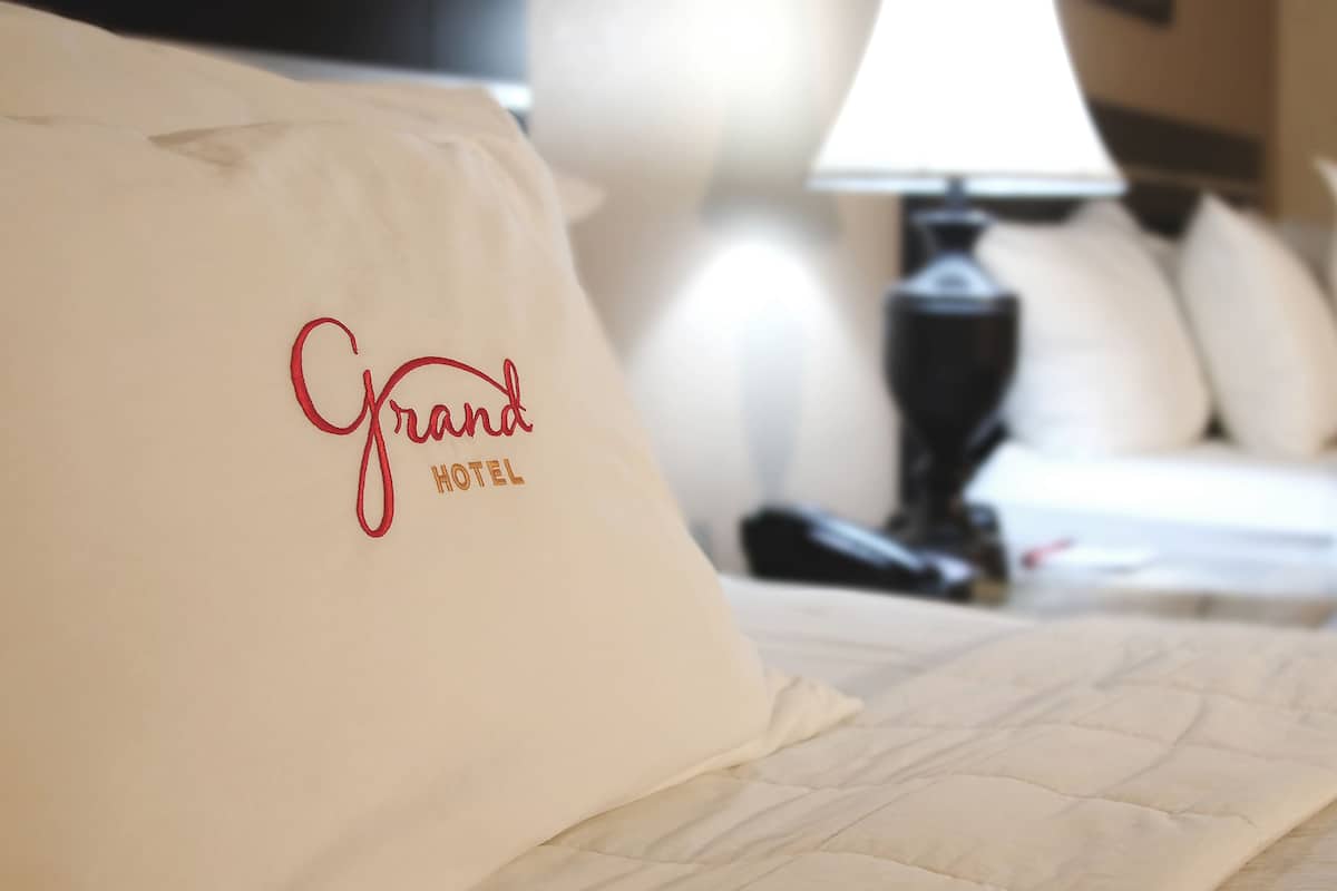 Una cama de hotel con un cojín que dice "Grand Hotel" y una lámpara de noche.