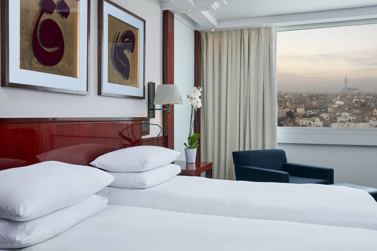 Une chambre d’hôtel avec un lit, une chaise, une table de chevet, une lampe et une vue sur le paysage urbain.