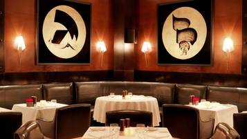 Un restaurante con cabinas de cuero y mesas redondas, cada una con manteles blancos y velas.