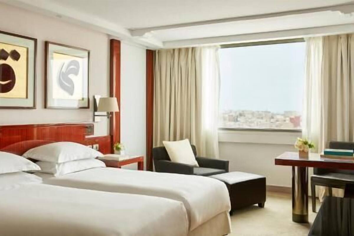 Une chambre d’hôtel avec deux lits, un bureau, une chaise, une lampe et une vue sur le paysage urbain.