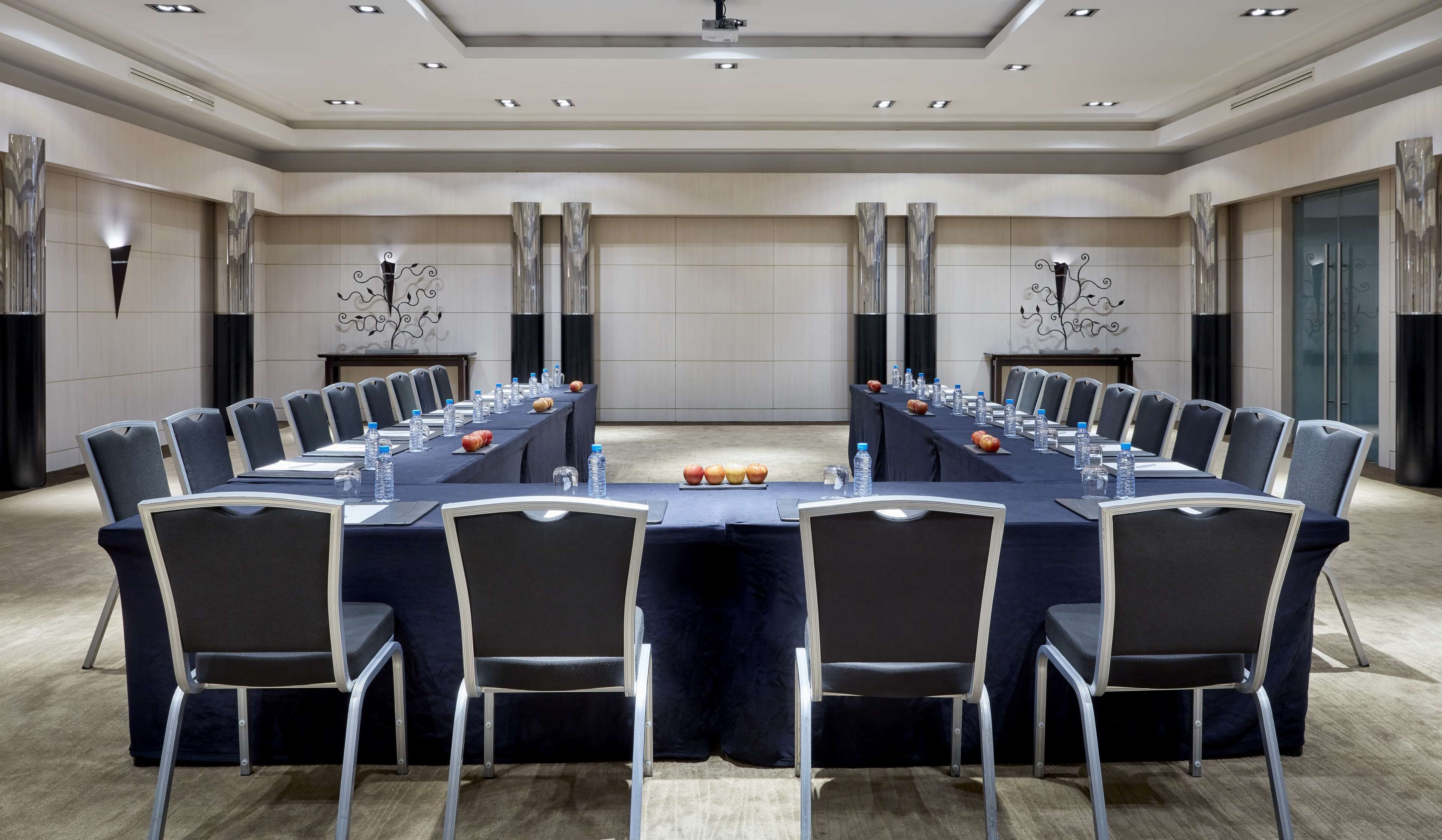 Sala de conferência com uma mesa comprida, cadeiras, garrafas de água e maçãs.