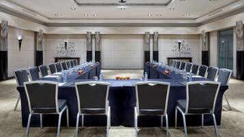 Sala de conferência com uma mesa comprida, cadeiras, garrafas de água e maçãs.