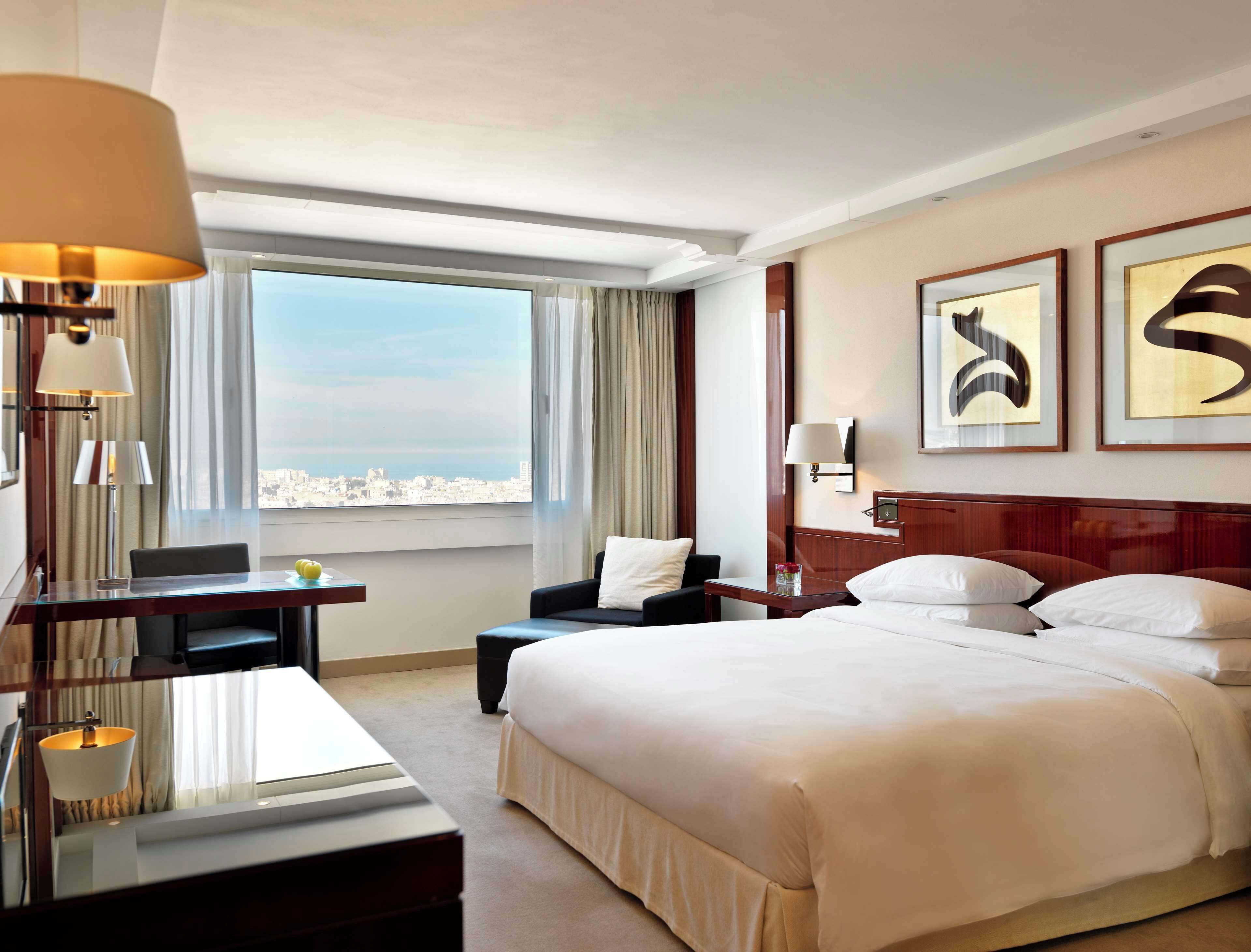 Habitación de hotel con una cama grande, un escritorio, una silla y vistas a la ciudad.