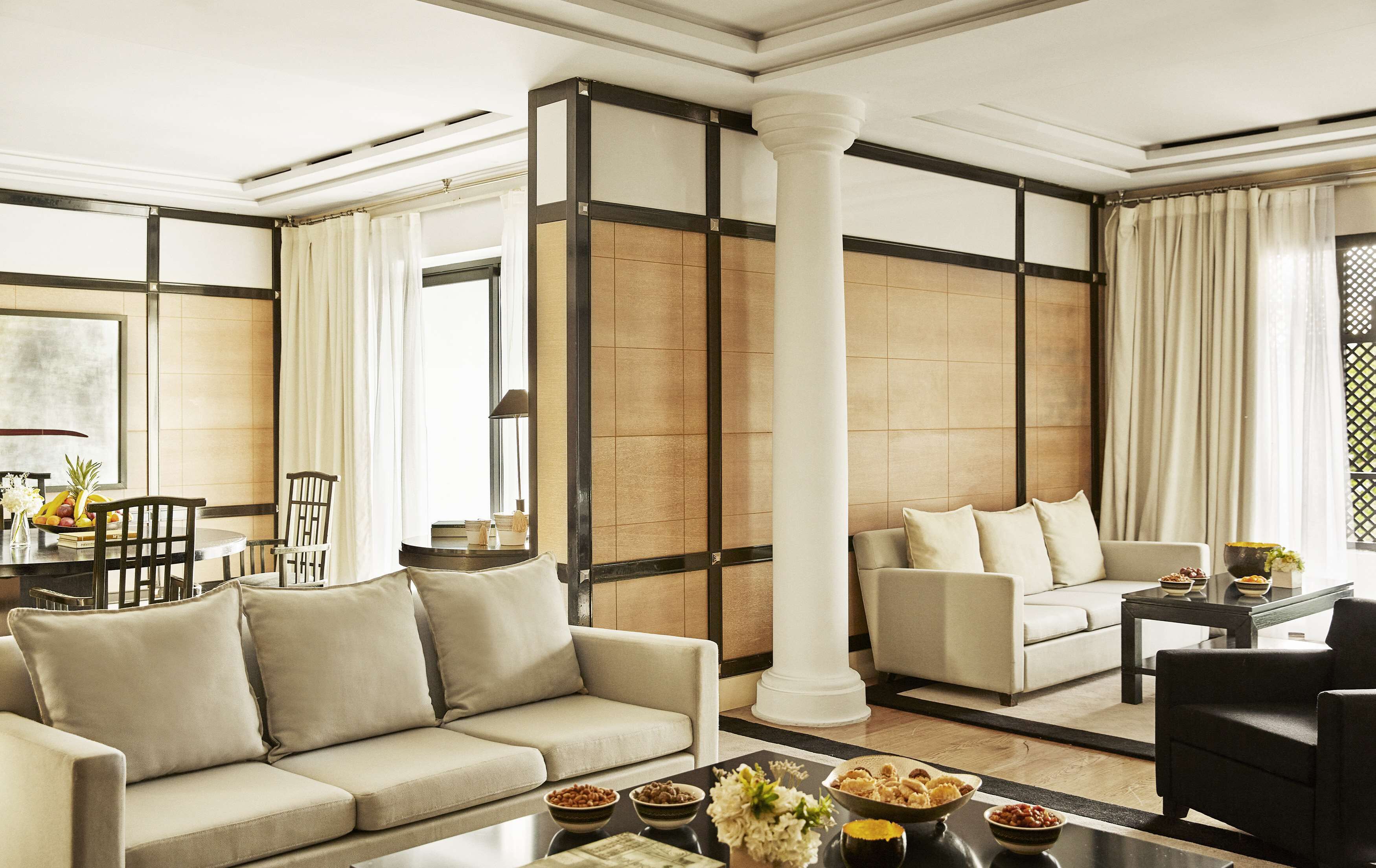 A modern living room with a sofa, armchairs, a coffee table, and a dining area with a table and chairs.