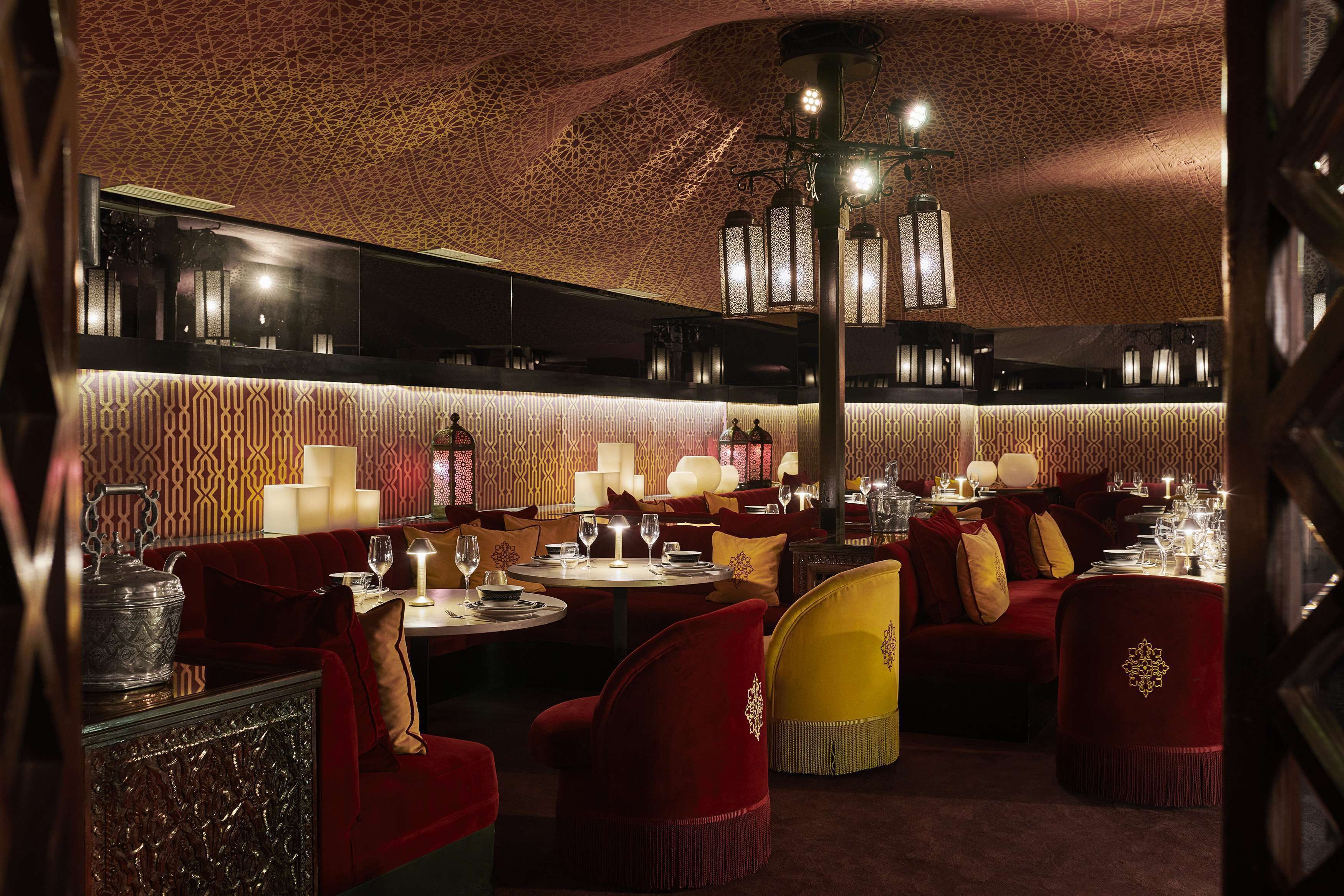 A restaurant with round tables, red and yellow upholstered chairs, and patterned walls.