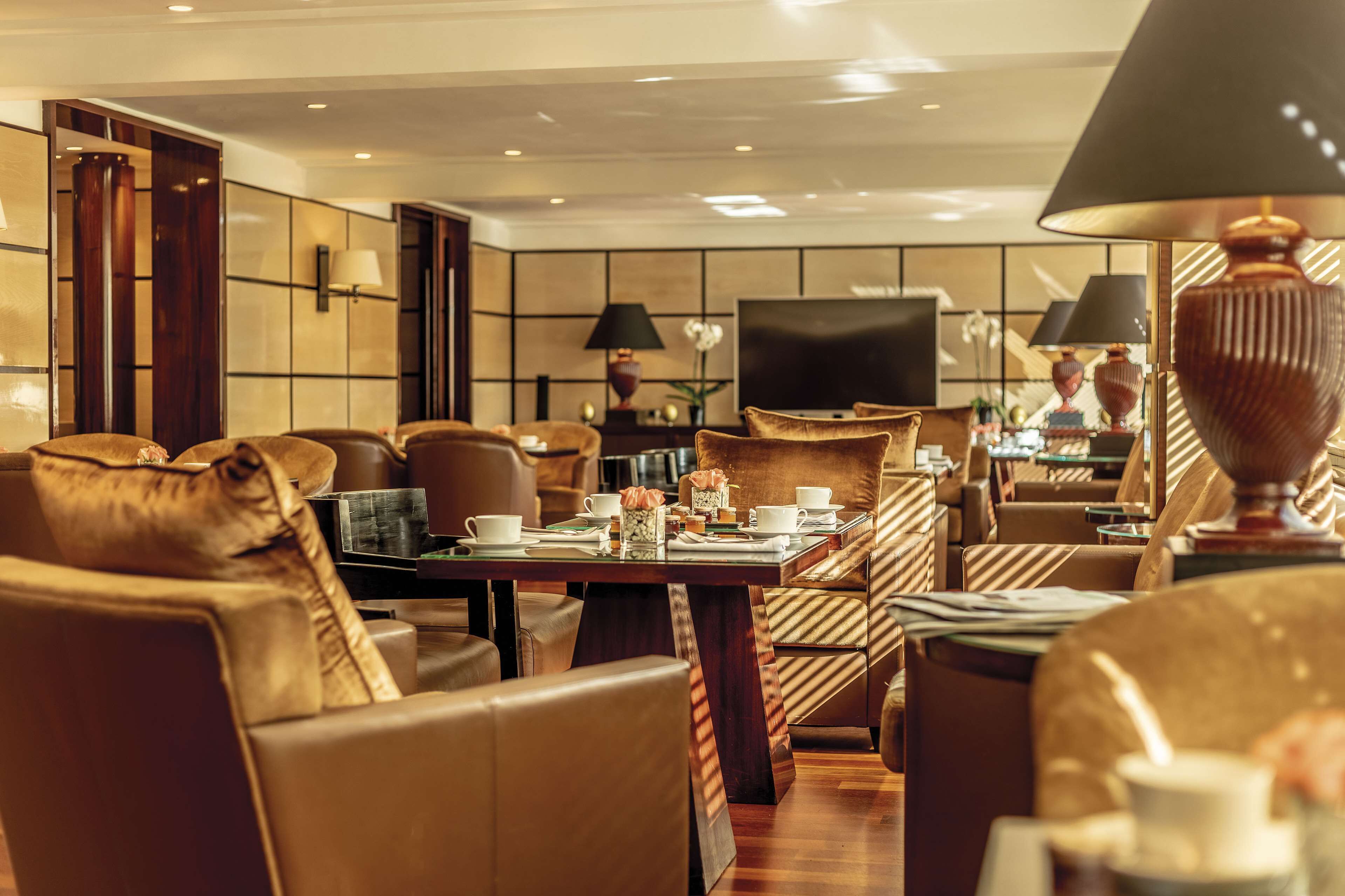 Un hall d’hôtel moderne avec des fauteuils en cuir, une grande table à manger centrale et un grand téléviseur à écran plat.