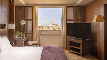 A hotel room with a bed, TV, and a view of a cityscape.